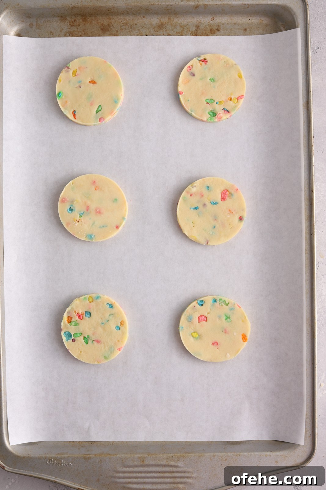 Fruity Pebbles Cookies Recipe: Colorful, Crispy Treats 7 A baking sheet lined with parchment paper with round cut out cookies on it.