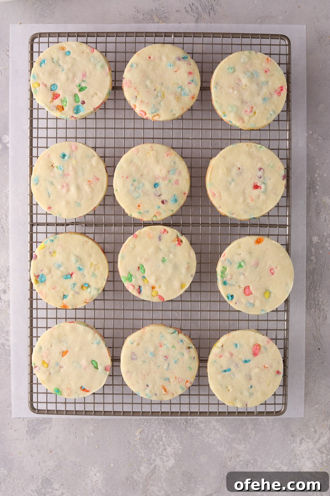 Fruity Pebbles Cookies Recipe: Colorful, Crispy Treats 8 Round cookies on a baking rack with parchment paper under it.
