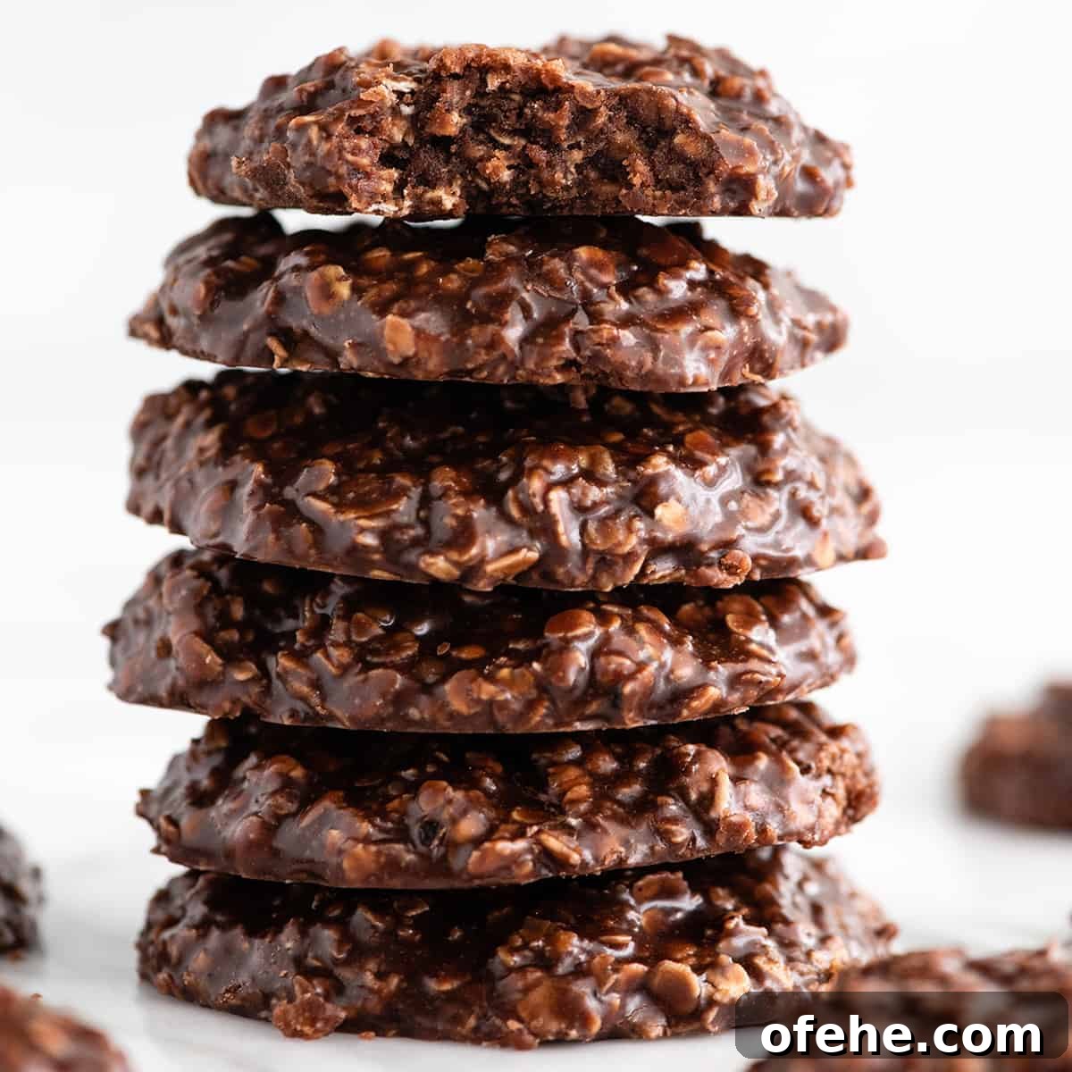 front view of a stack of 6 no bake cookies, the top one has a bite taken out of it so the fudgy texture is visible. The stack is surrounded by more no bake cookies!