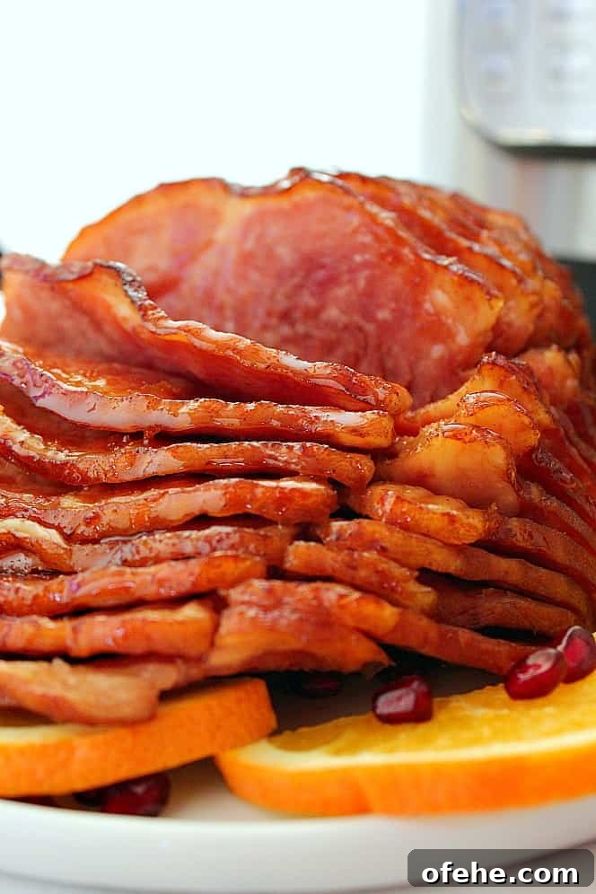 Instant Pot Honey-Orange Glazed Ham - spiral-cut ham cooked in 10 minutes in the Instant Pot, glazed with sweet and delicious honey citrus glaze with cinnamon and cloves. Close up shot of glazed sliced ham on white serving platter.