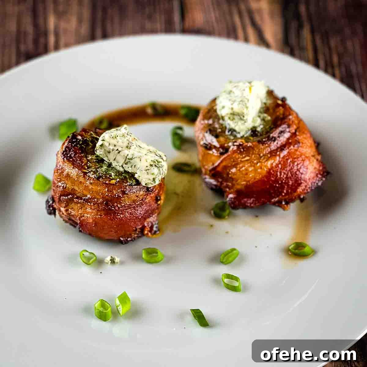 Crispy Bacon-Wrapped Filet Mignon in the Air Fryer 11 The two filet mignon steaks on a white plate, sprinkled with green onion and topped with compound butter.