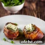 Crispy Bacon-Wrapped Filet Mignon in the Air Fryer 19 Two air fried filet mignon with bacon on a white plate with garlic herb compound butter on top.