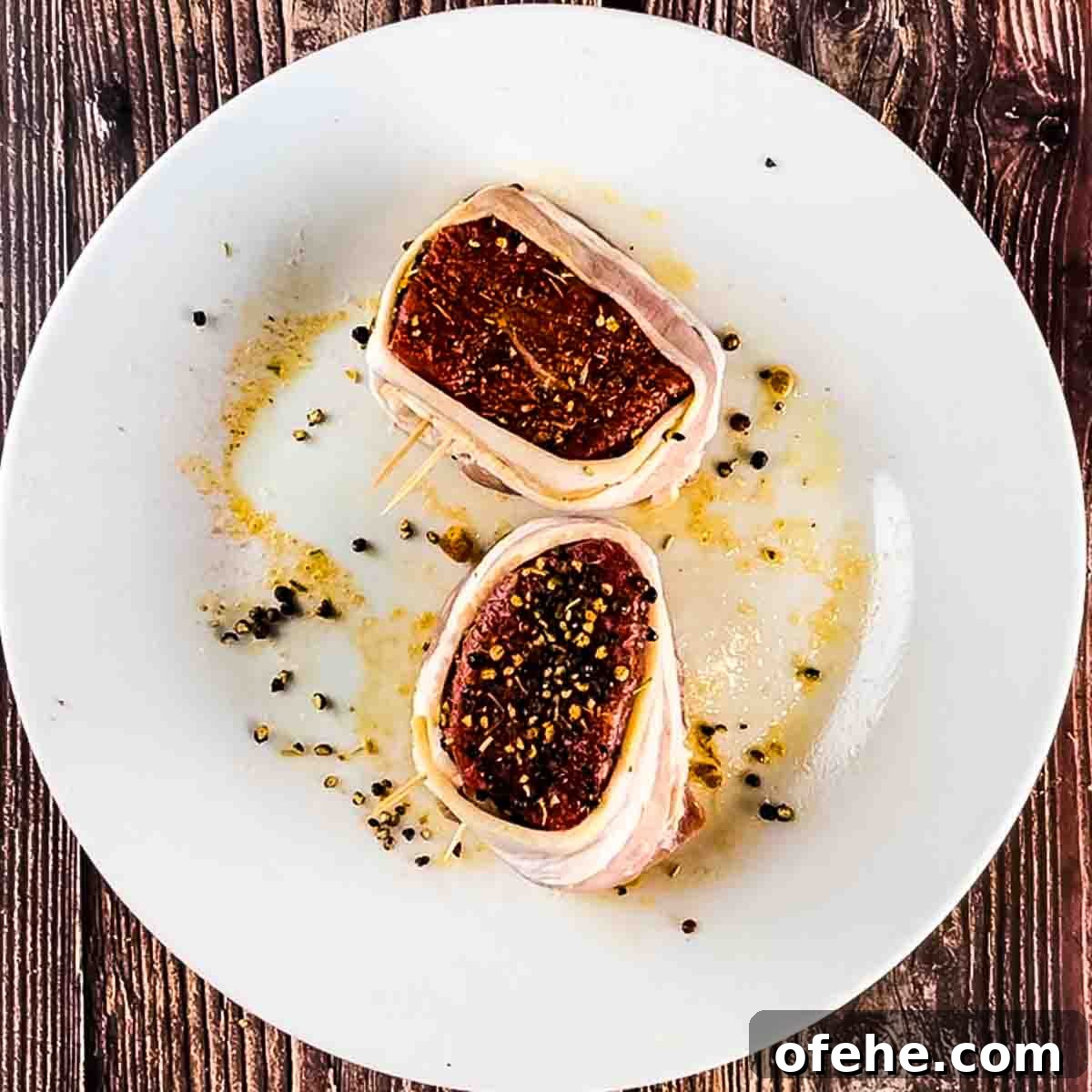 Crispy Bacon-Wrapped Filet Mignon in the Air Fryer 7 The filet mignon on a white plate with bacon wrapped around each one.