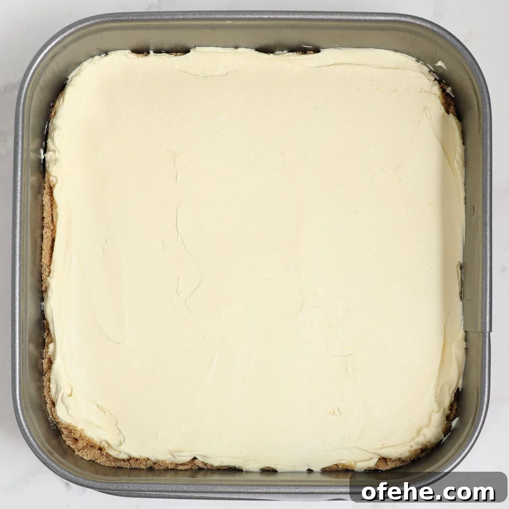 A square metal baking pan filled with blueberry lemon delight—layers of smooth, creamy, pale topping spread evenly over a crumbly brown crust.
