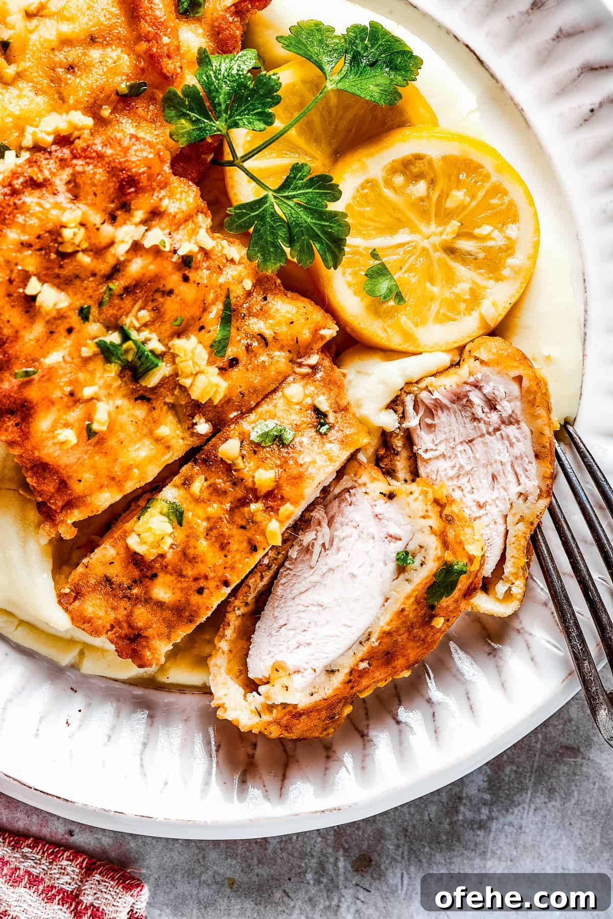 Wondering what to make for dinner? Try this easy Lemon Chicken Recipe! Crispy, parmesan-crusted chicken with real lemon butter sauce. Yum! Sliced Breaded chicken with parsley and lemon slices placed next to it.