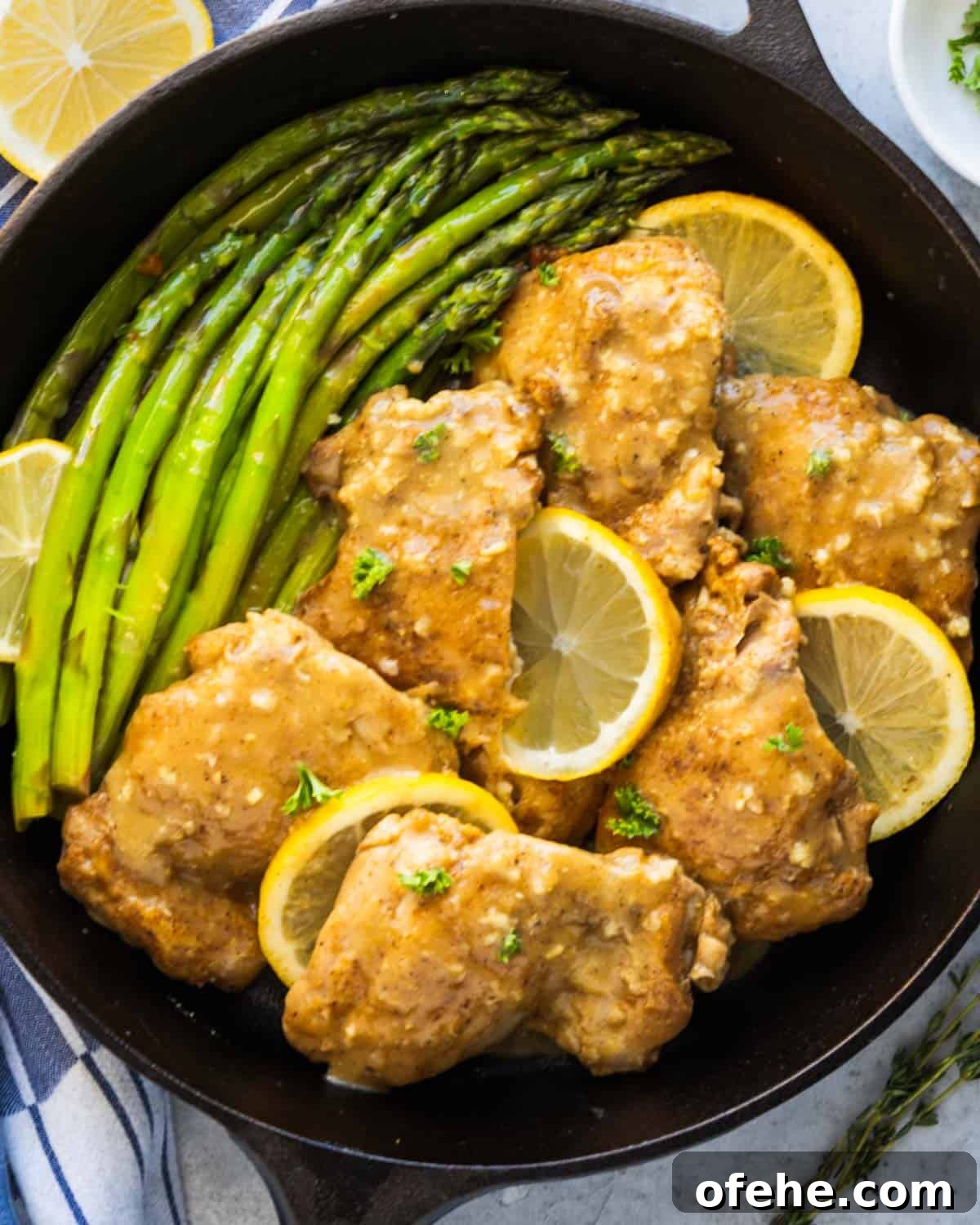 a black pan with chicken, slices of lemons and asparagus
