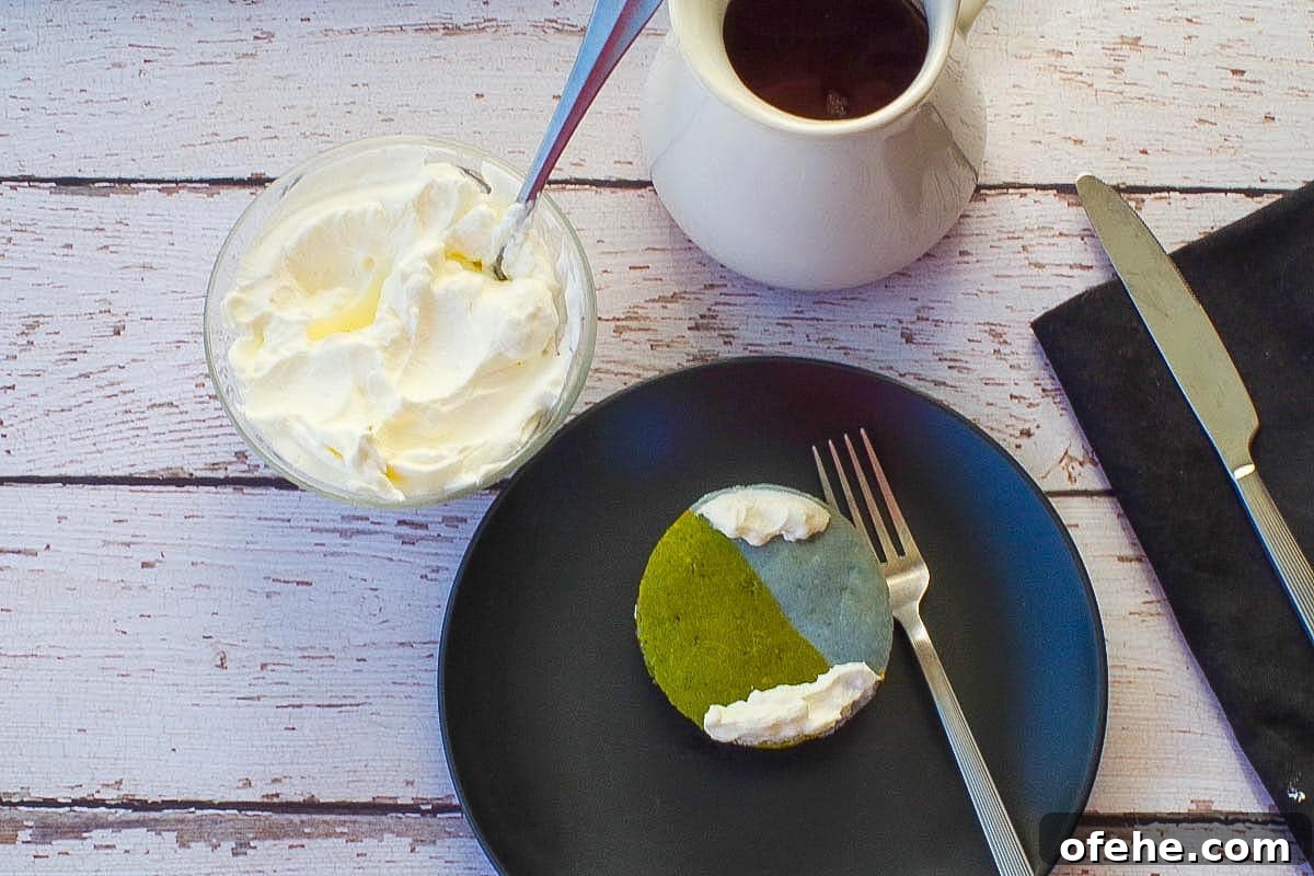 Colorful Earth Day Sheet-Pan Pancakes Recipe 18 Sheet Pan Easy Earth Day Pancake cut into a round globe on a black plate with whipped cream and syrup in the background.