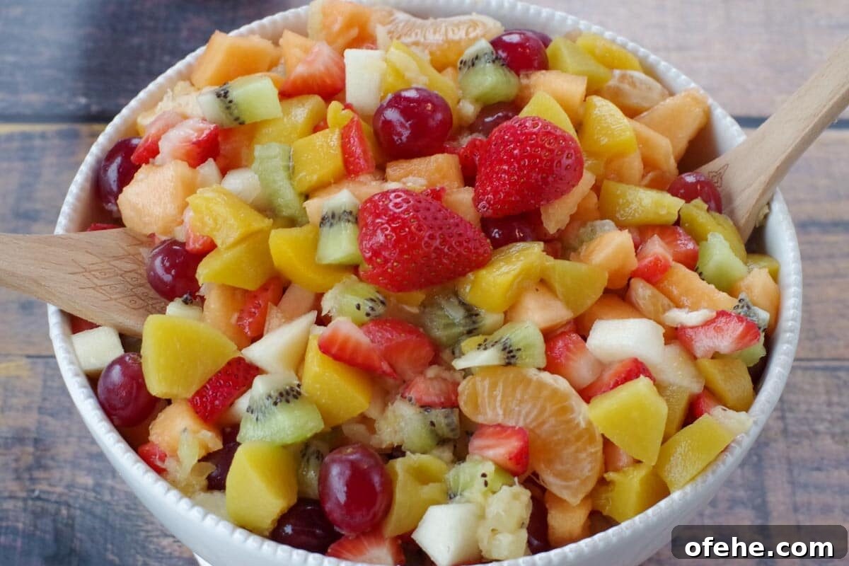 Colorful Earth Day Sheet-Pan Pancakes Recipe 19 classic fruit salad in a white bowl with wooden serving spoons on each side (on faux wooden surface)