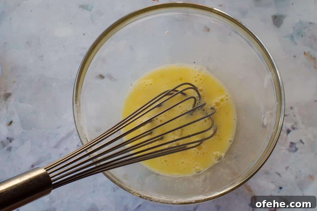 Colorful Earth Day Sheet-Pan Pancakes Recipe 5 Egg being whisked with whisk in glass bowl.