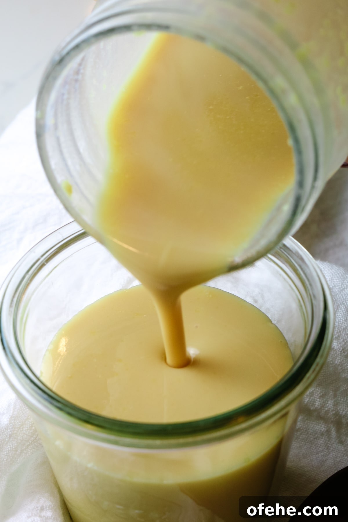 condensed milk being poured from mason jar into another glass jar.