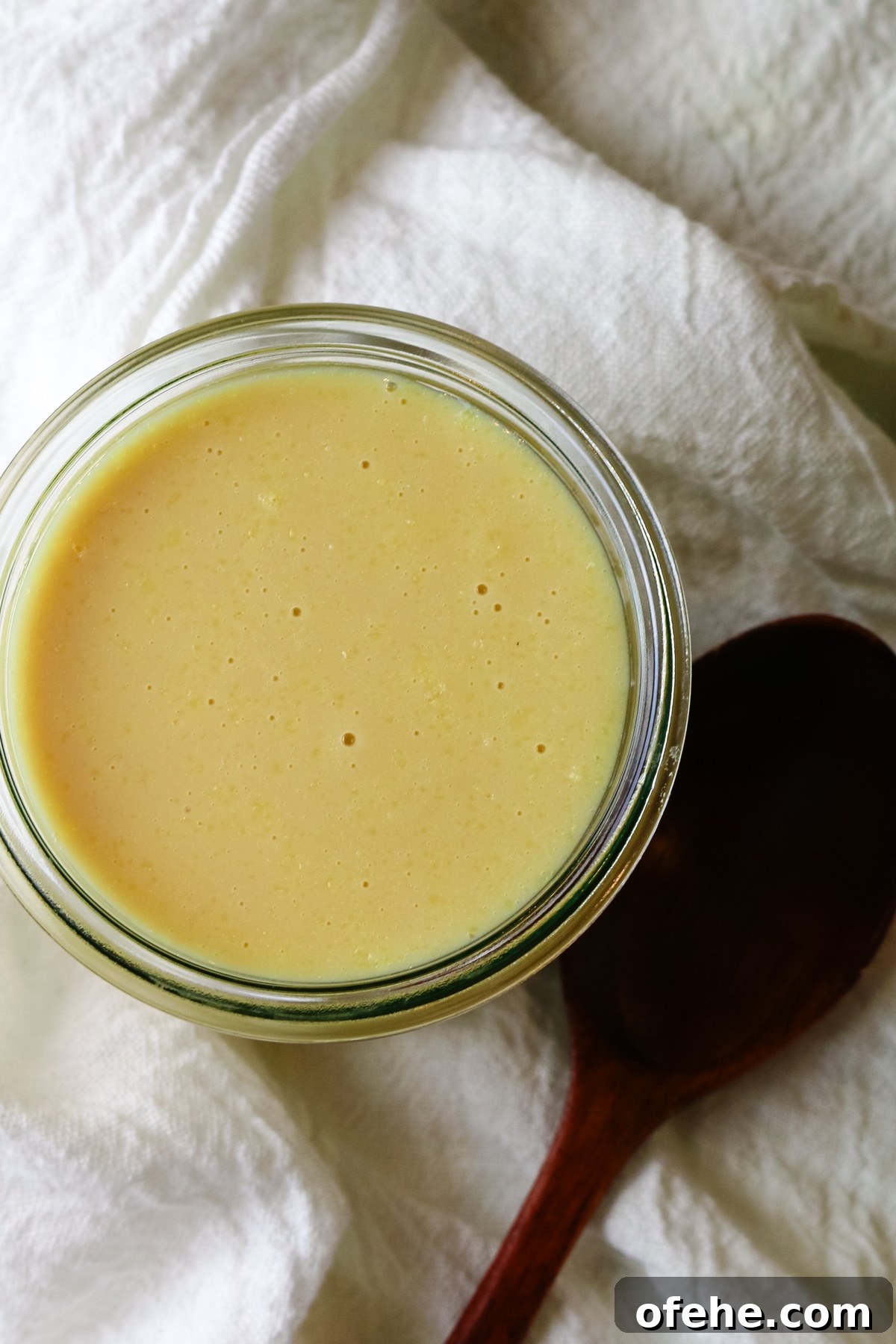 a wooden spoon next to a glass jar filled with condensed milk.