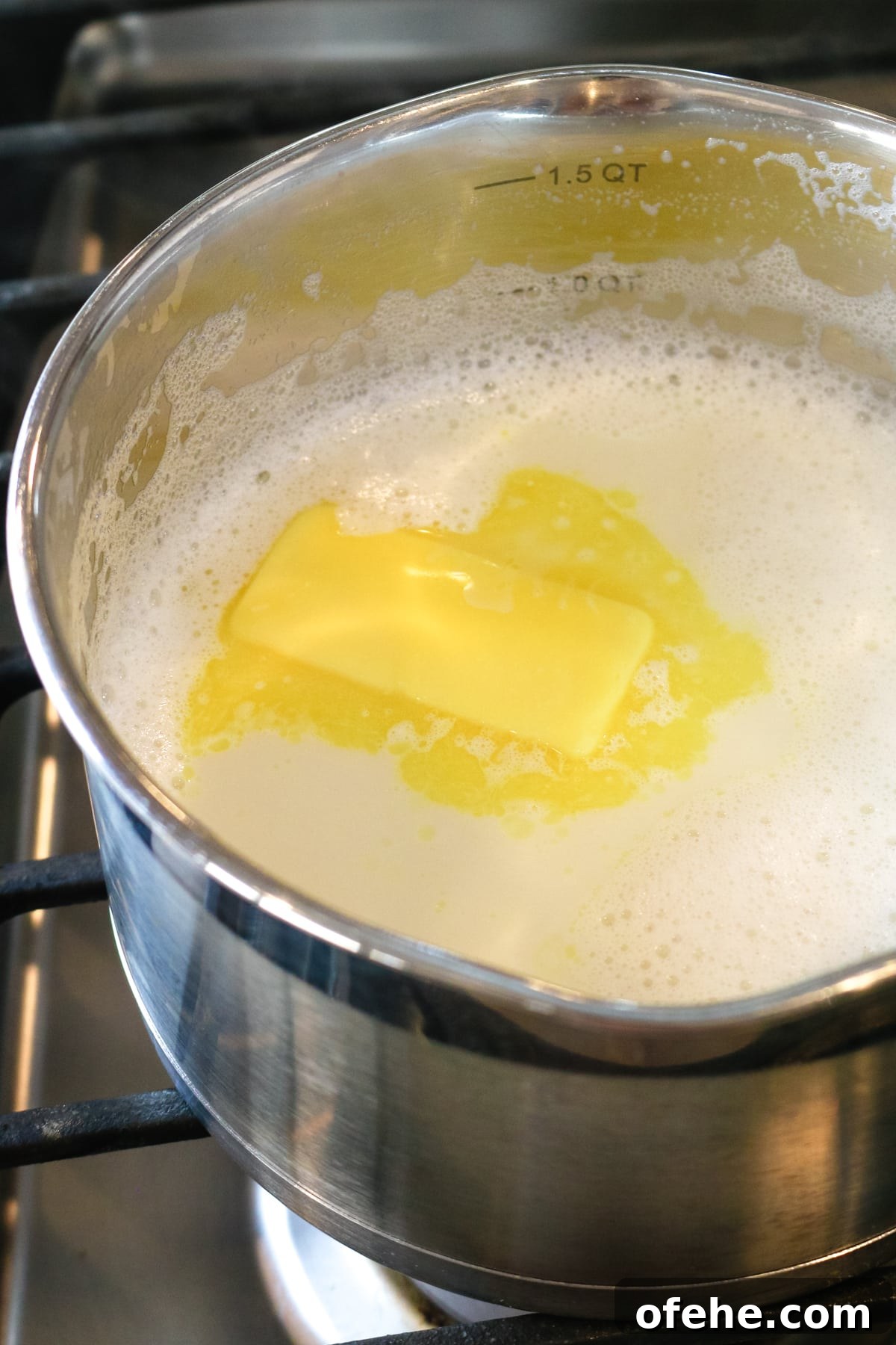 whisked milk inside of a metal pan with a slice of butter inside of it.