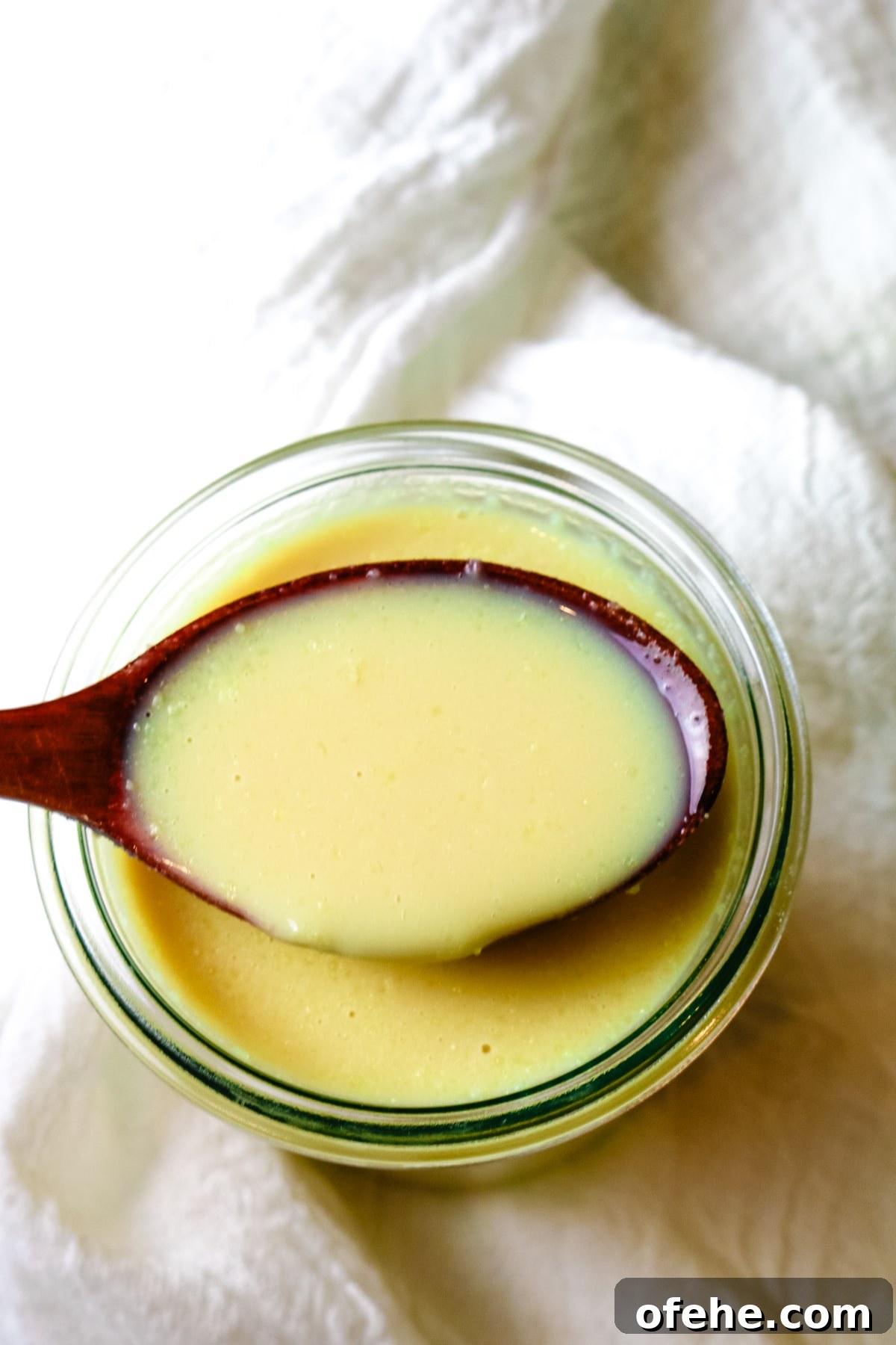 a glass jar filled with condensed milk and a wooden spoon with some condensed milk on it over the jar.