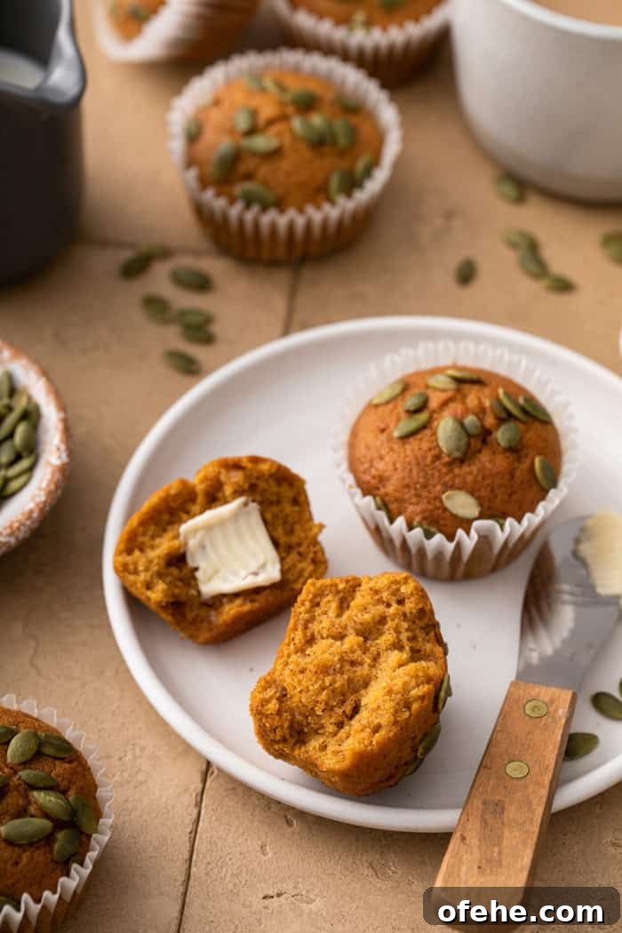 Moist Pumpkin Muffins with Warm Spices Recipe 9 Two pumpkin muffins on a white plate. One muffin is split in half with butter on one half