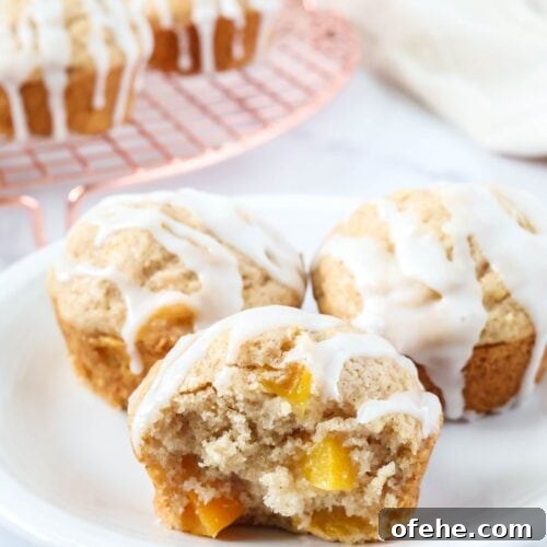 Peach Muffins Made with Bisquick — Quick Summer Treat 11 Three peach muffins made with Bisquick served on a white plate, with more muffins on a wire rack in the background.