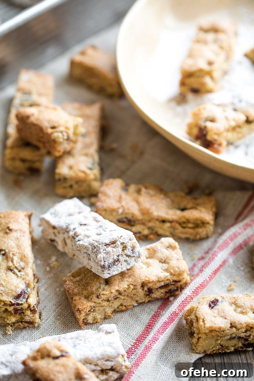 Lots of bars scattered on a vintage-looking cloth, some already dipped in sugar and some not, with the sugar bowl in the background.