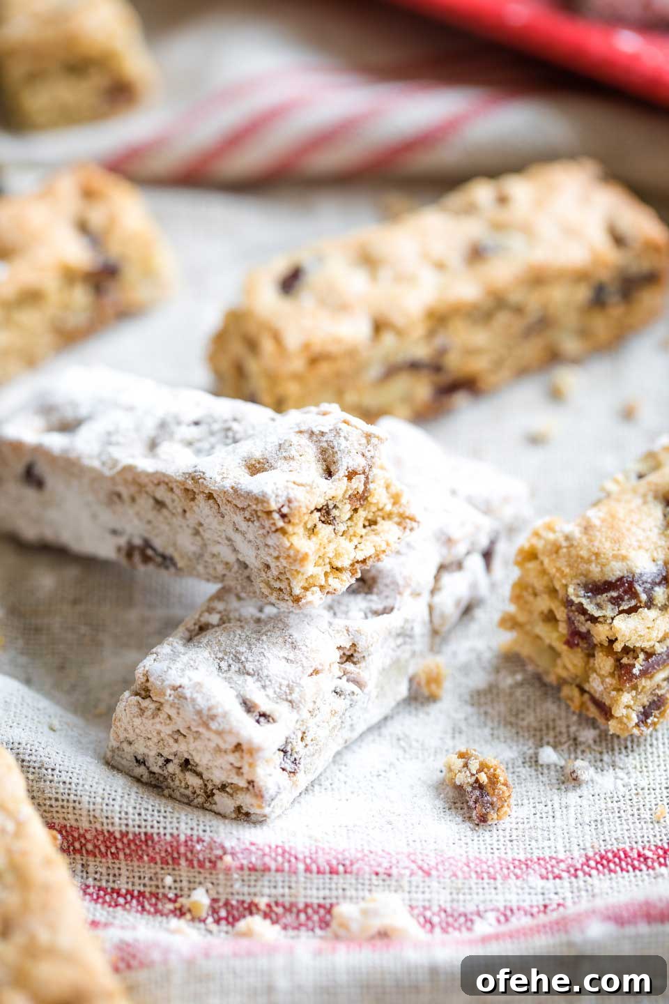 Closeup of two sugared Date Nut Bars leaning on each other, with un-sugared ones surrounding them on a vintage-looking cloth.