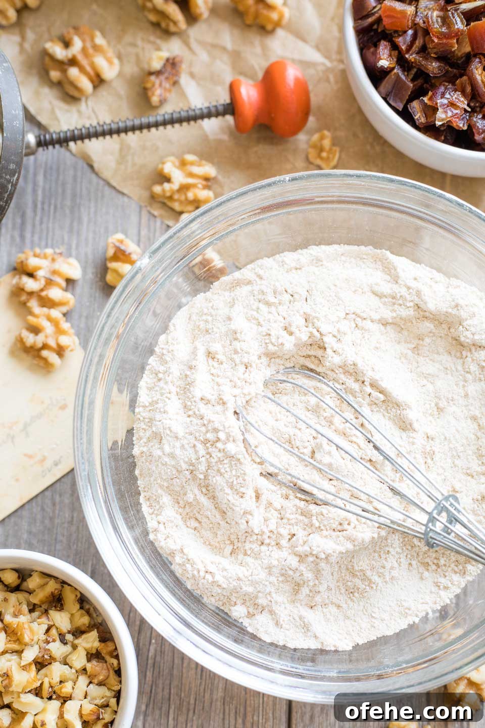 Overhead photo of the dry ingredients in a glass mixing bowl, with nuts and dates surrounding it.
