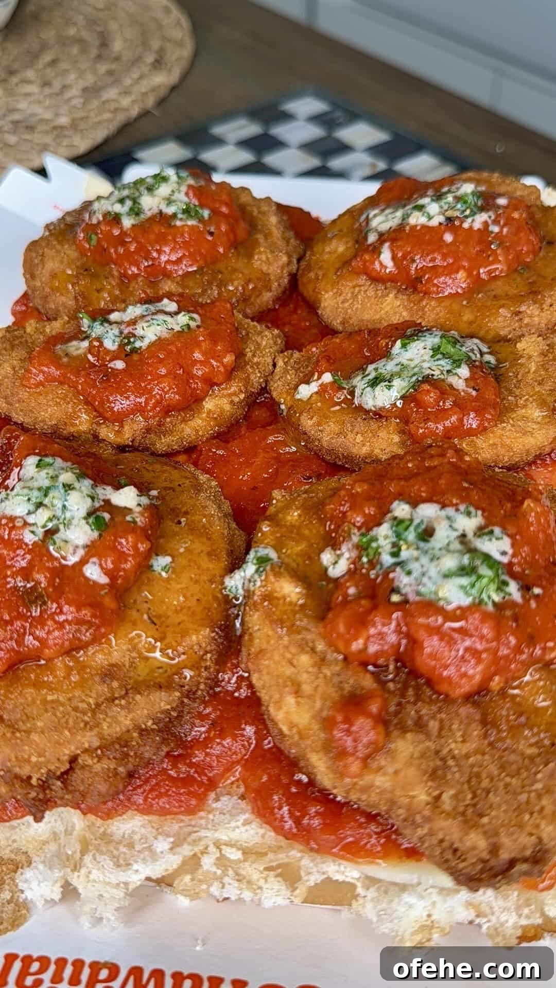 Close-up of several breaded and fried chicken cutlets topped with tomato sauce and a sprinkle of green herbs, served on a sandwich roll. The food looks crispy and saucy, ready to eat.
