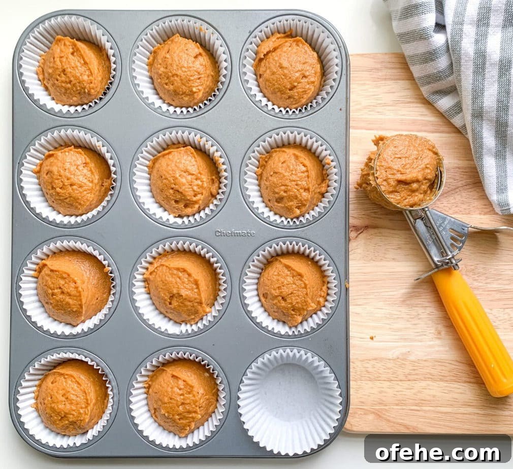 Pumpkin Streusel Muffins with Cinnamon Crunch Topping 5 A muffin pan with pumpkin batter in all but one cup. A cookie scoop full of batter is off to the side.