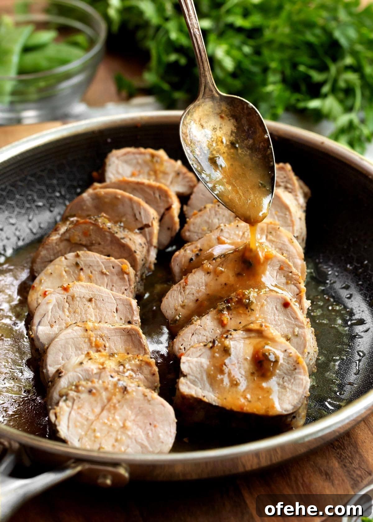 Juicy Oven-Roasted Pork Tenderloin Recipe 2 2 Pork Tenderloins sliced in a skillet with spoon drizzling sauce on them.