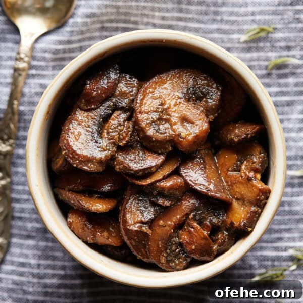 Overhead photo of browned sliced mushrooms in a small bowl on a striped cloth.