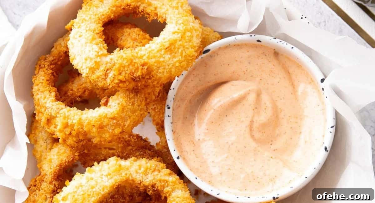 Overhead image of air fryer onion rings with sauce in small bowl on the side.