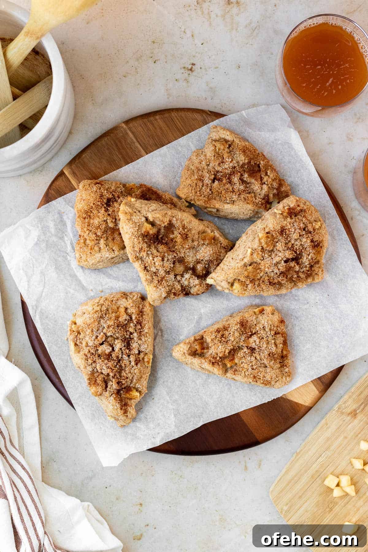 Apple Cinnamon Scones with Crunchy Cinnamon Streusel Topping 2 apple cinnamon scones sit atop a parchment lined round wood cutting board