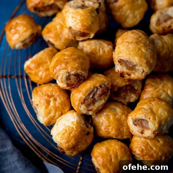 Crispy Chicken Lollipops Recipe: Finger-Licking Party Snack 11 A pile of golden-brown sausage rolls rests on a wire cooling tray, showing flaky pastry and browned meat filling.