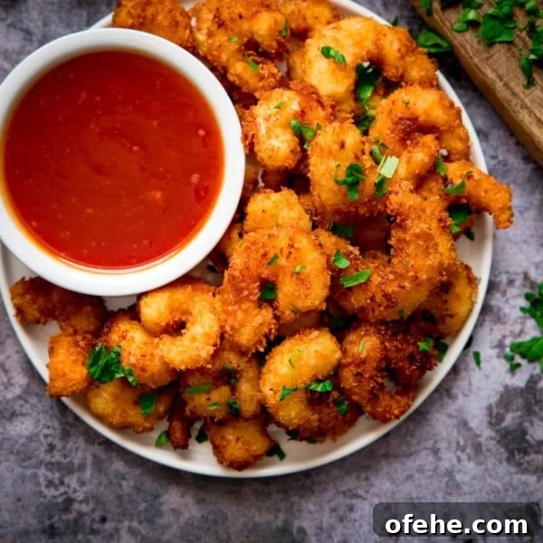 Crispy Chicken Lollipops Recipe: Finger-Licking Party Snack 12 Plate of coconut shrimp with a bowl of sweet and sour sauce nestled in. Plate is on a grey background.