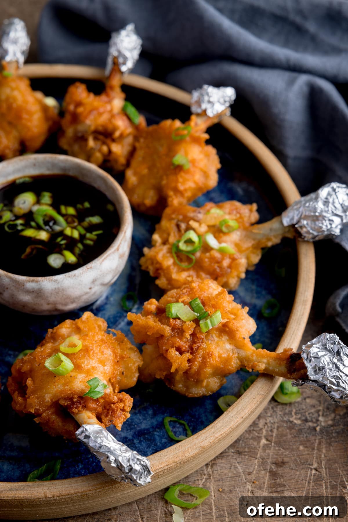 Crispy Chicken Lollipops Recipe: Finger-Licking Party Snack 15 Close up side image of chicken lollipops arranged in a circle on a blue plate with a dipping bowl of sticky spicy sauce int he middle.