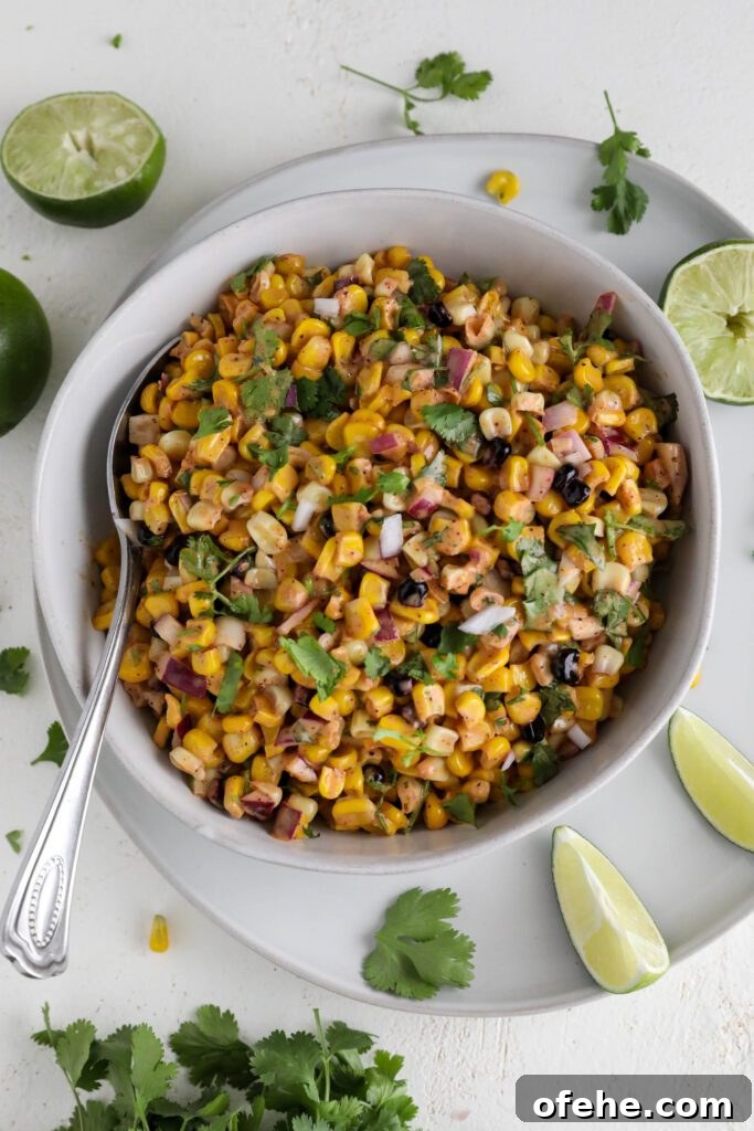 Vegan Elote Corn Salad served in bowl with spoon surrounded by cilantro and limes 