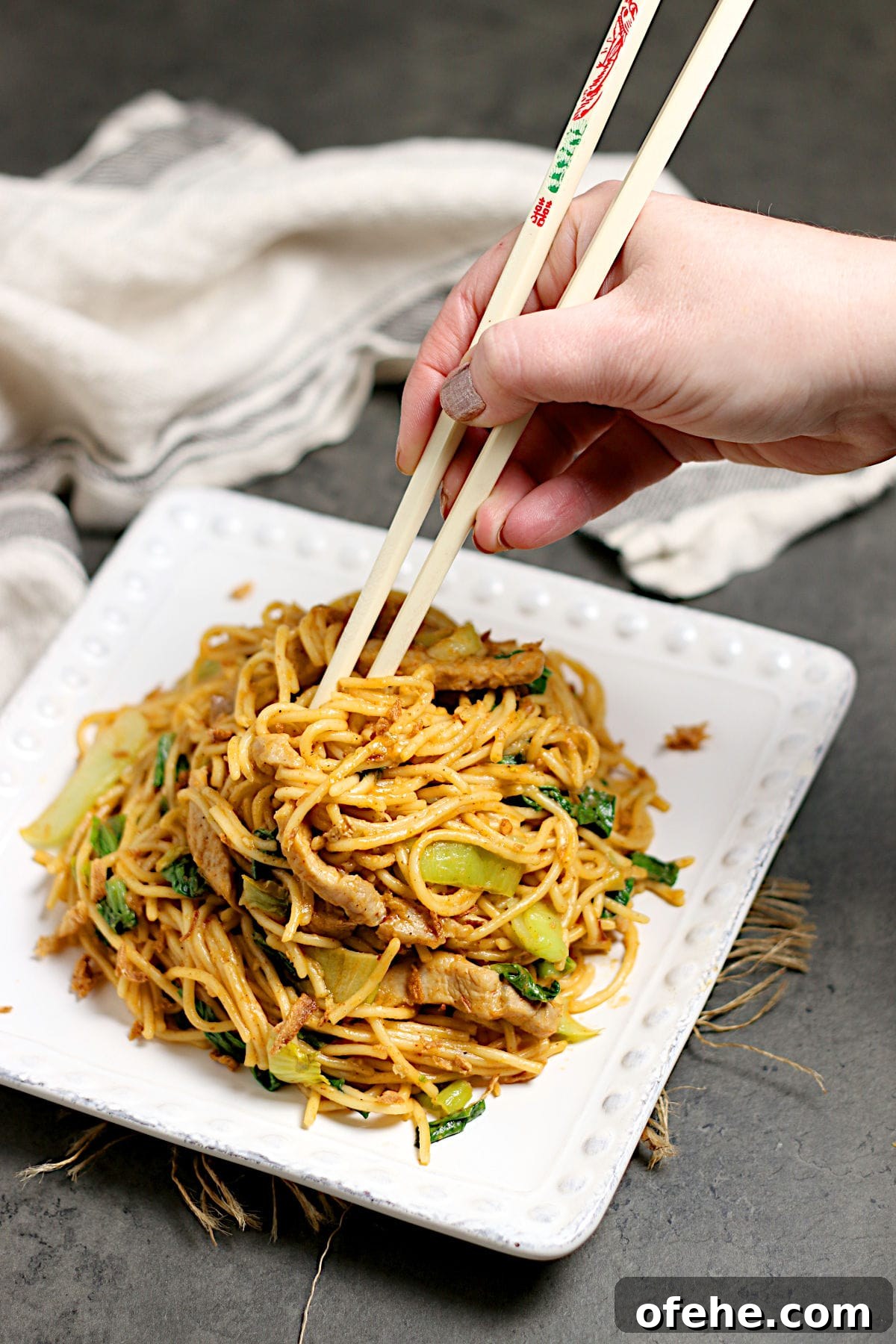 Sichuan-Style Spicy Pork Noodles with Bok Choy 5 A hand grabbing some Spicy Noodles with Pork and Bok Choy from a plate with chopsticks.