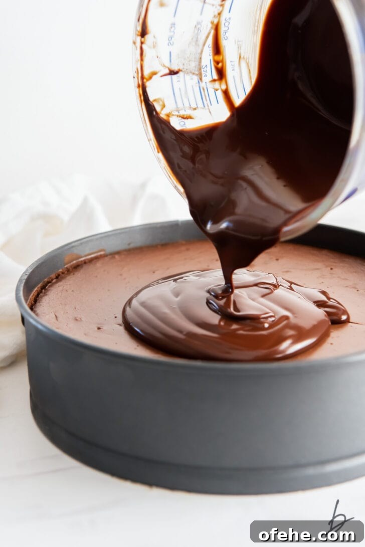 chocolate ganache being poured on top of chocolate cheesecake in a springform pan