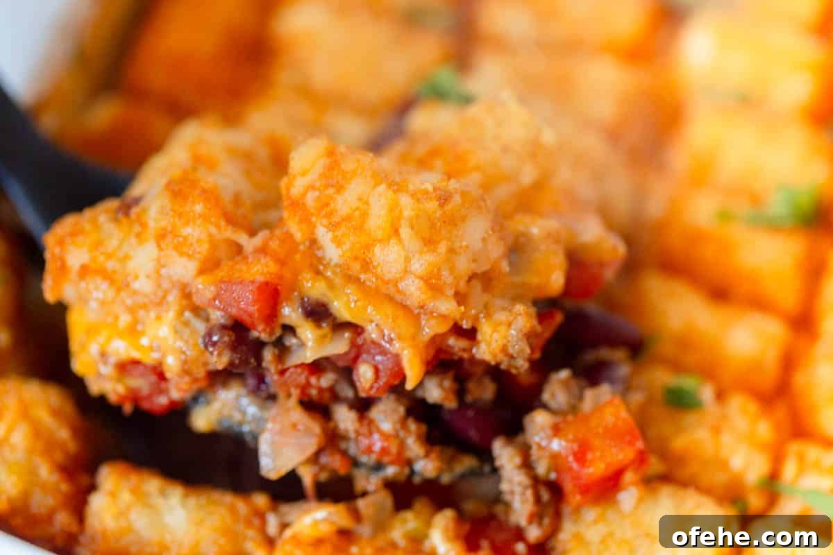 A pan of chili tater tot casserole with a black serving spoon taking a big scoop out.