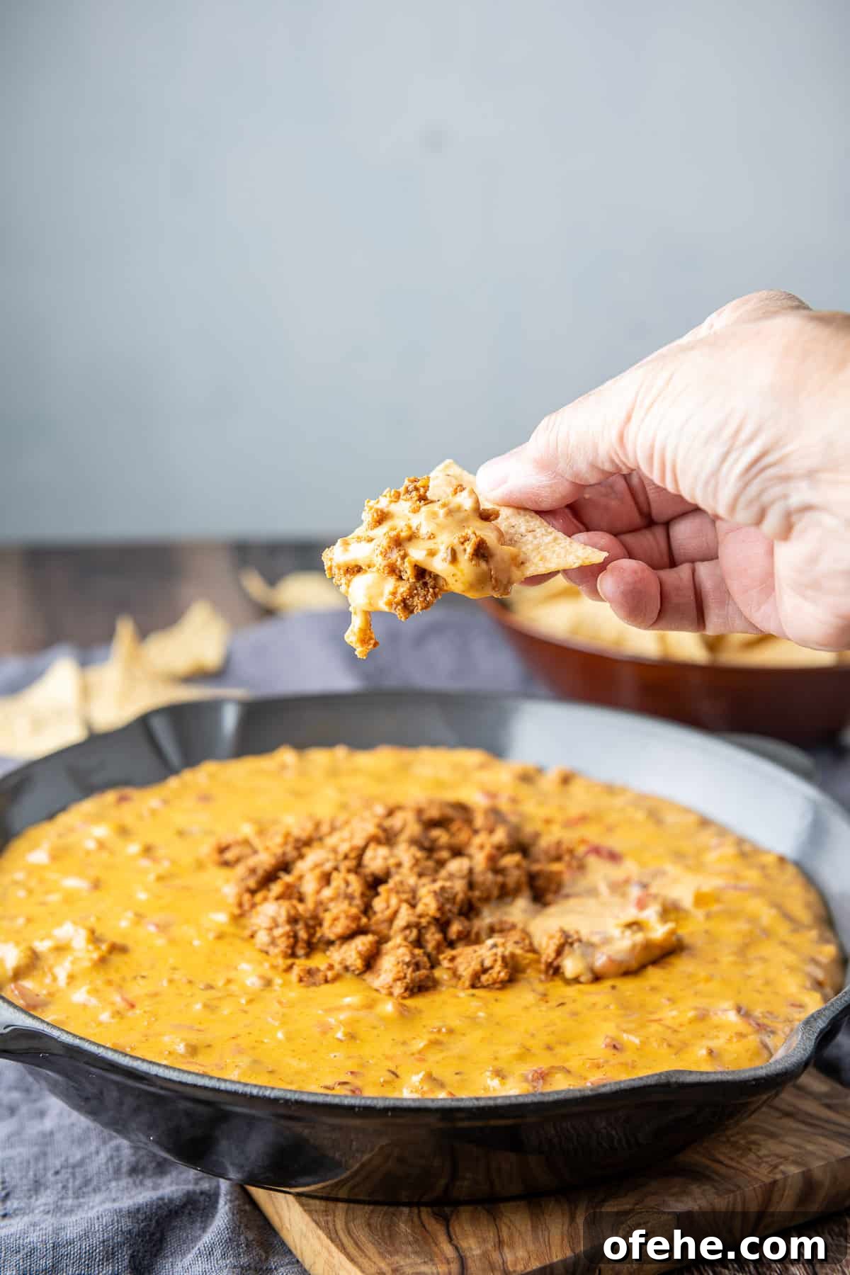 Creamy Chorizo Dip Recipe for Game Day or Parties 9 A hand holding a chip with the chorizo dip on it, held over the pan