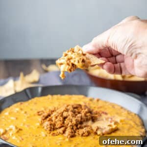 Creamy Chorizo Dip Recipe for Game Day or Parties 10 square photo of a hand holding a chip with the cheese dip on it