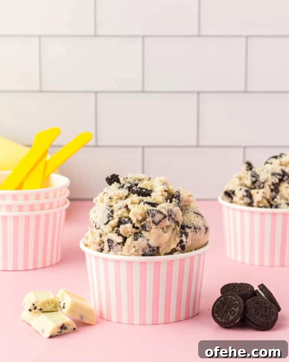 Edible Oreo Cookie Dough Recipe You Can Eat Raw 2 side view of servings of oreo cookie dough piled into pink and white striped paper cups.