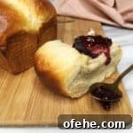 Brioche bun with jam, the rest of the brioche, a spoon with jam in the background.