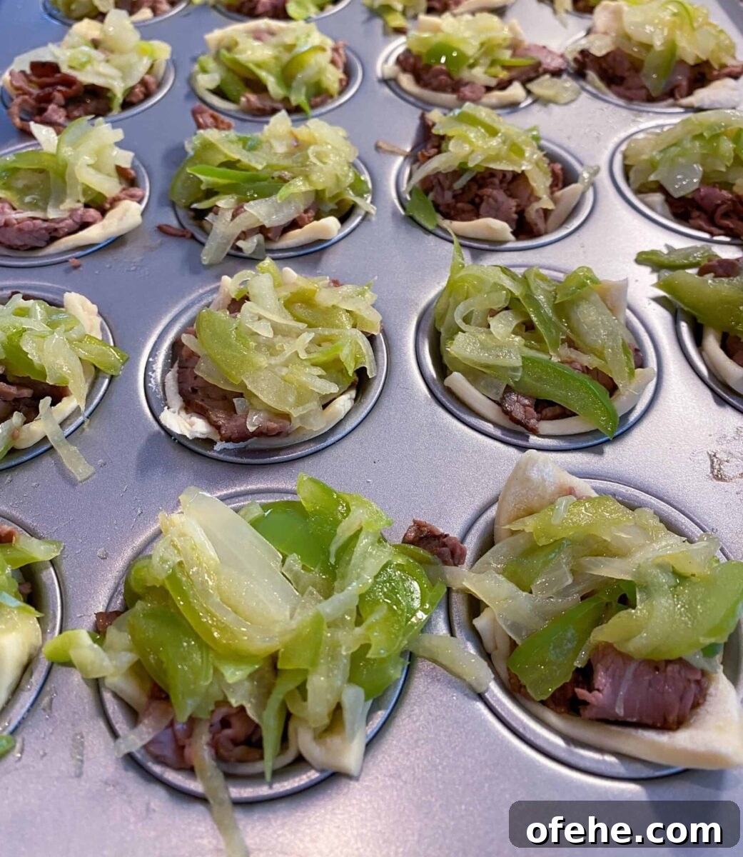Philly Cheesesteak Bites Recipe: Savory Mini Sandwich Appetizers 7 Mini Philly Cheesesteaks in a mini-muffin pan with cooked veggies on top of each one.