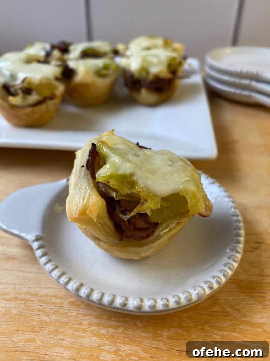 Philly Cheesesteak Bites Recipe: Savory Mini Sandwich Appetizers 8 A Philly Cheesesteak Bite on a small plate, with a larger plate in the background and additional bites on display.