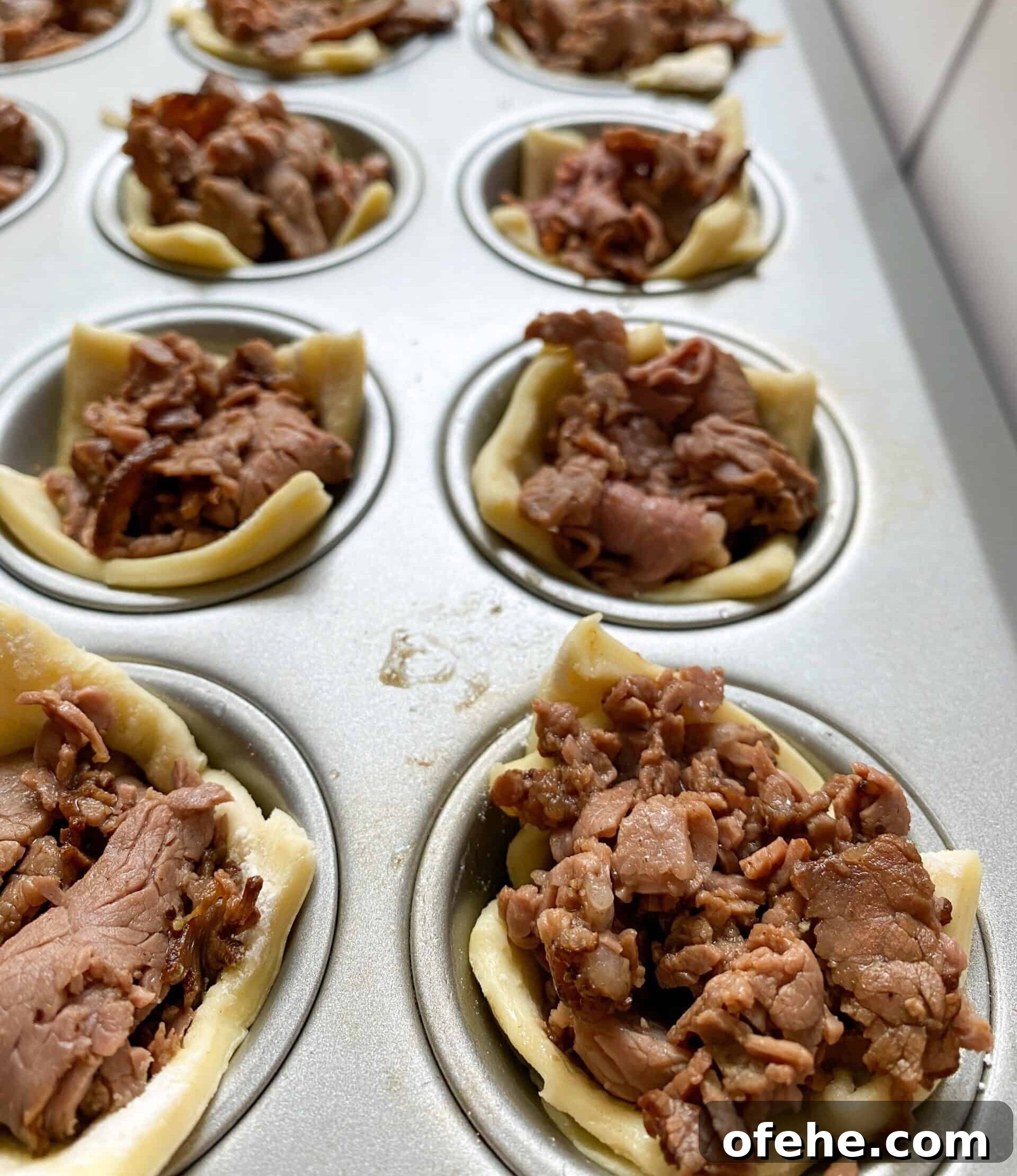 Philly Cheesesteak Bites Recipe: Savory Mini Sandwich Appetizers 9 Mini muffin cups with cooked roast beef and puffed pastry in each one.
