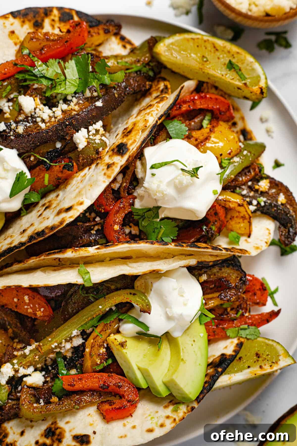 Oven-Baked Fajita Vegetables with Bell Peppers and Onions 2 White plate with three fajitas topped with sour cream and fresh cilantro
