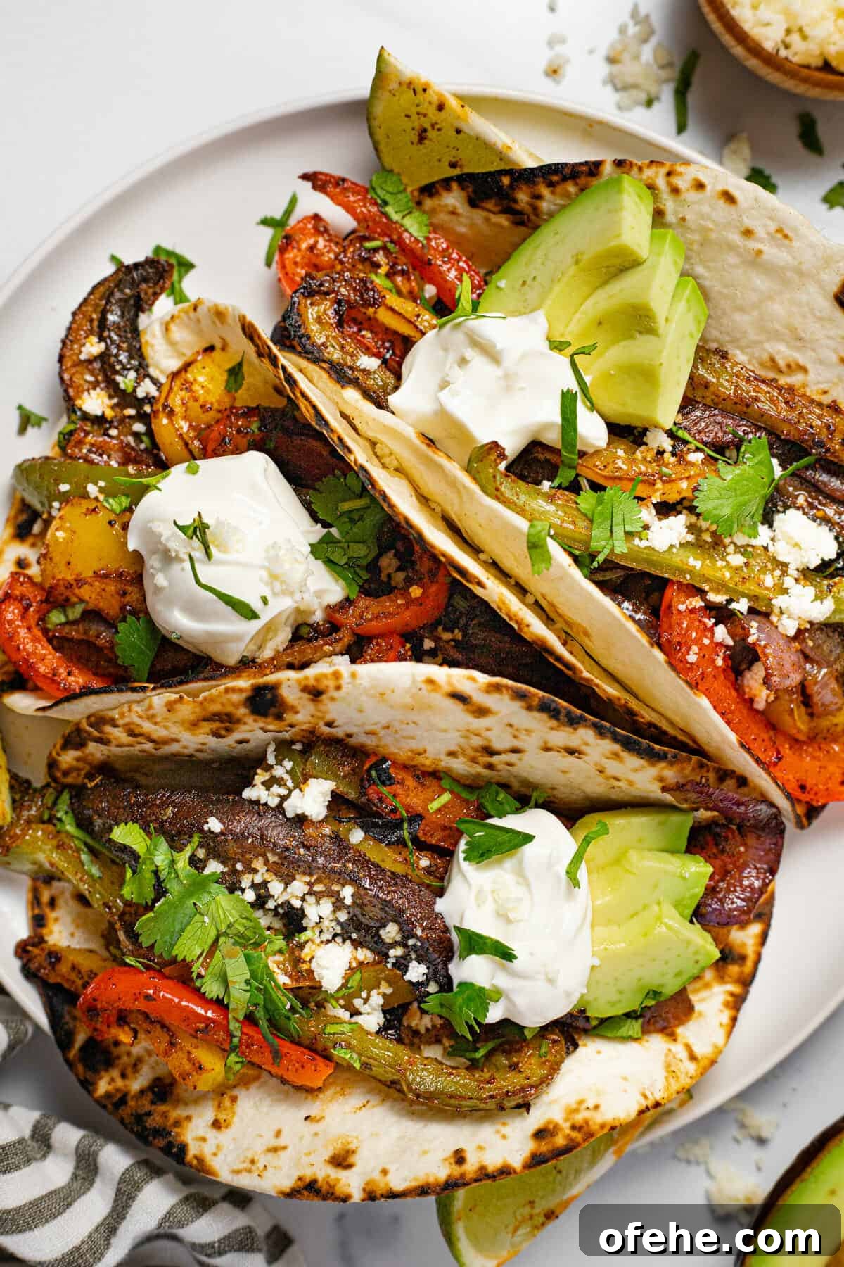 Oven-Baked Fajita Vegetables with Bell Peppers and Onions 9 White plate with three fajitas topped with sour cream and fresh cilantro