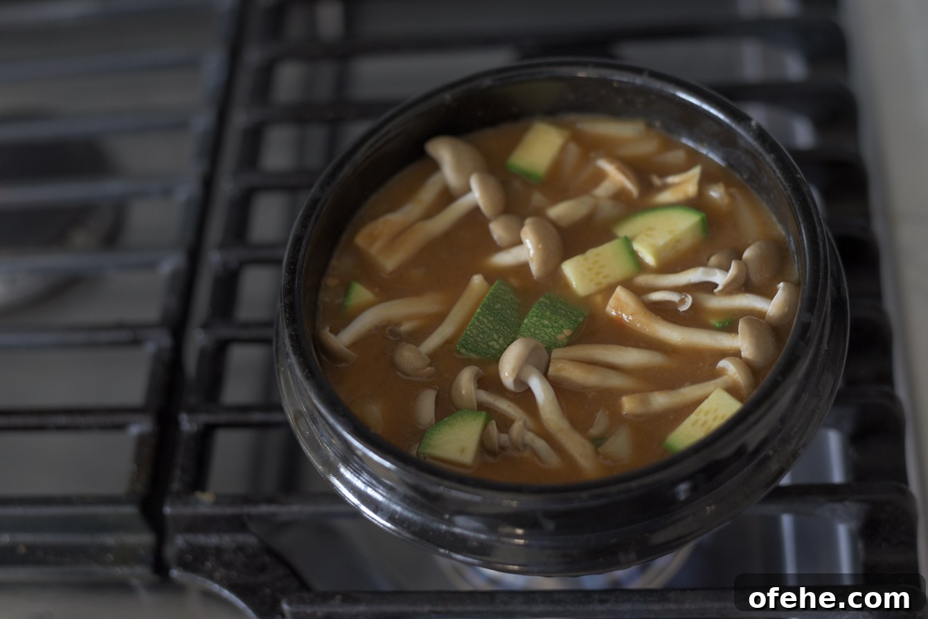 Authentic Doenjang Jjigae Recipe: Classic Korean Soybean Paste Stew 9 Adding sliced zucchini and mushrooms to a pot of simmering doenjang jjigae