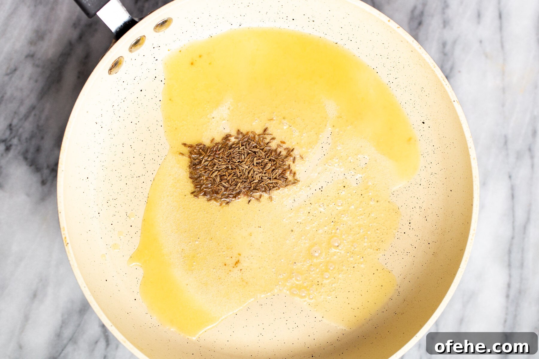 cumin seeds being fried in a frying pan 