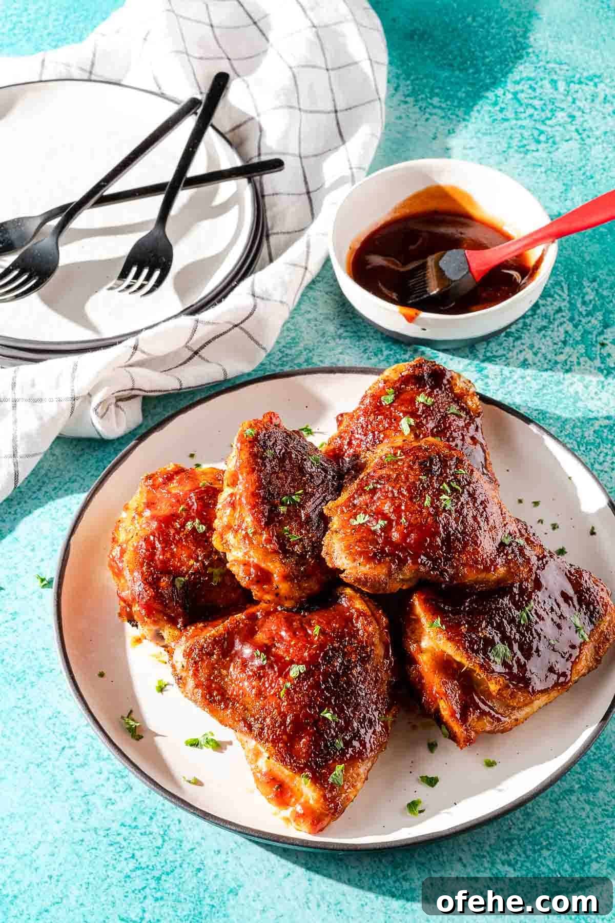 Juicy Baked BBQ Chicken Thighs with Crispy Skin 2 BBQ chicken thighs on plate with sauce and forks on the side