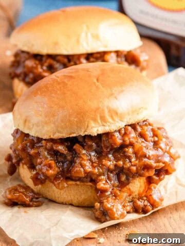 two bbq sloppy joes on board with bbq sauce on the side.