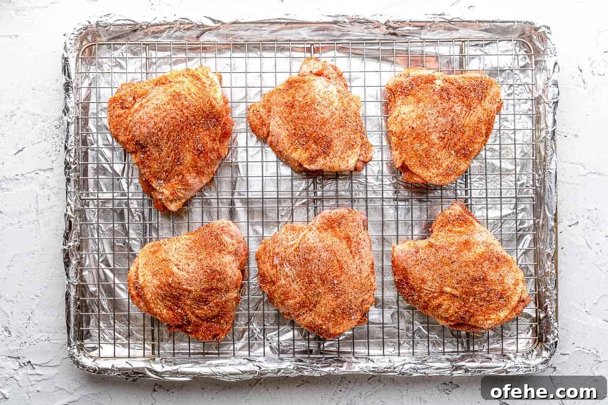Juicy Baked BBQ Chicken Thighs with Crispy Skin 9 seasoned chicken thighs on wire rack on baking sheet