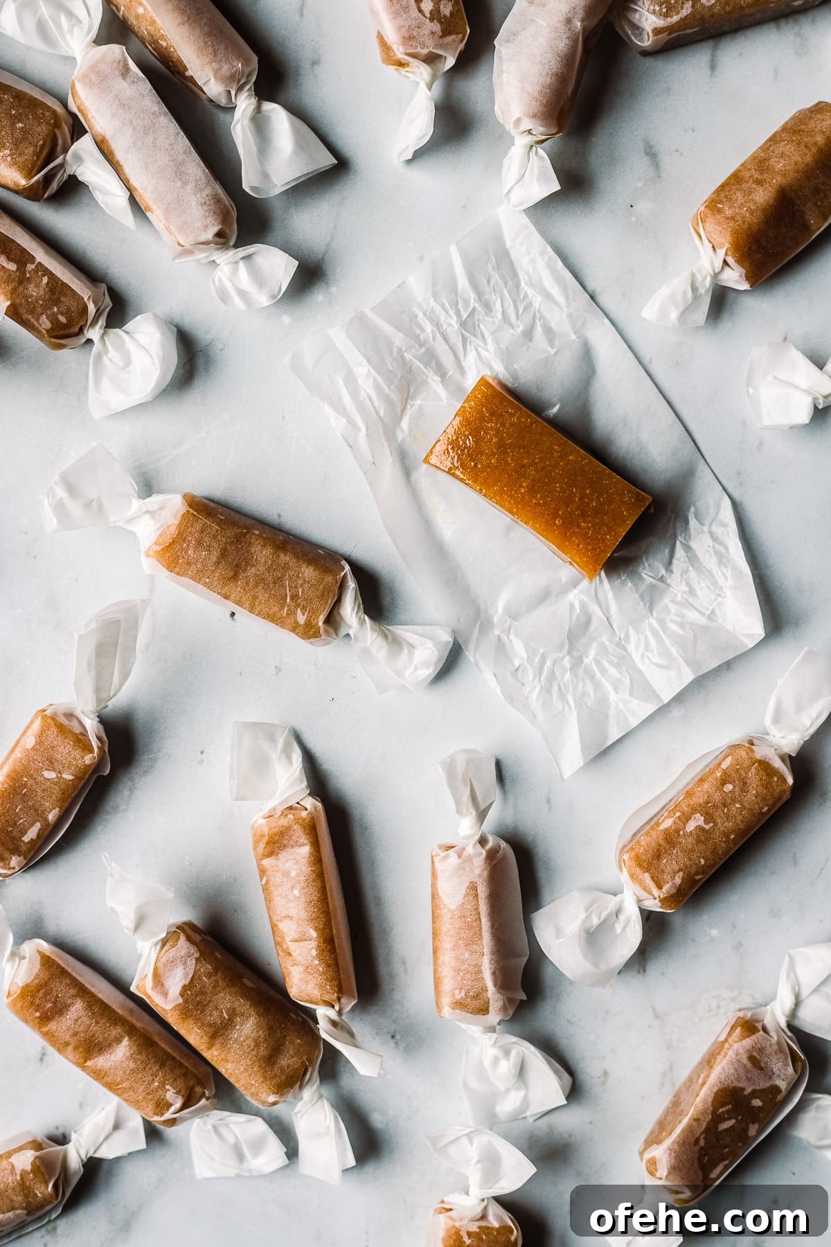 Individually wrapped whiskey salted caramels on a grey marble surface. One caramel is unwrapped.